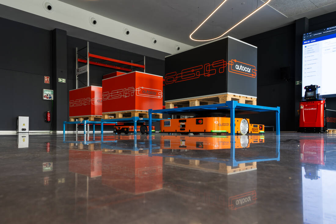 Showroom de Autocar en Orcoyen: vehículos de guiado automático moviendo palés bajo las estructuras azules.